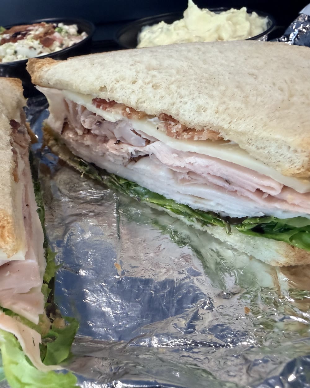 The Classic Club from Highland Square Deli, cut in half on foil, turkey and ham stacked under swiss and crisp bacon on white toast